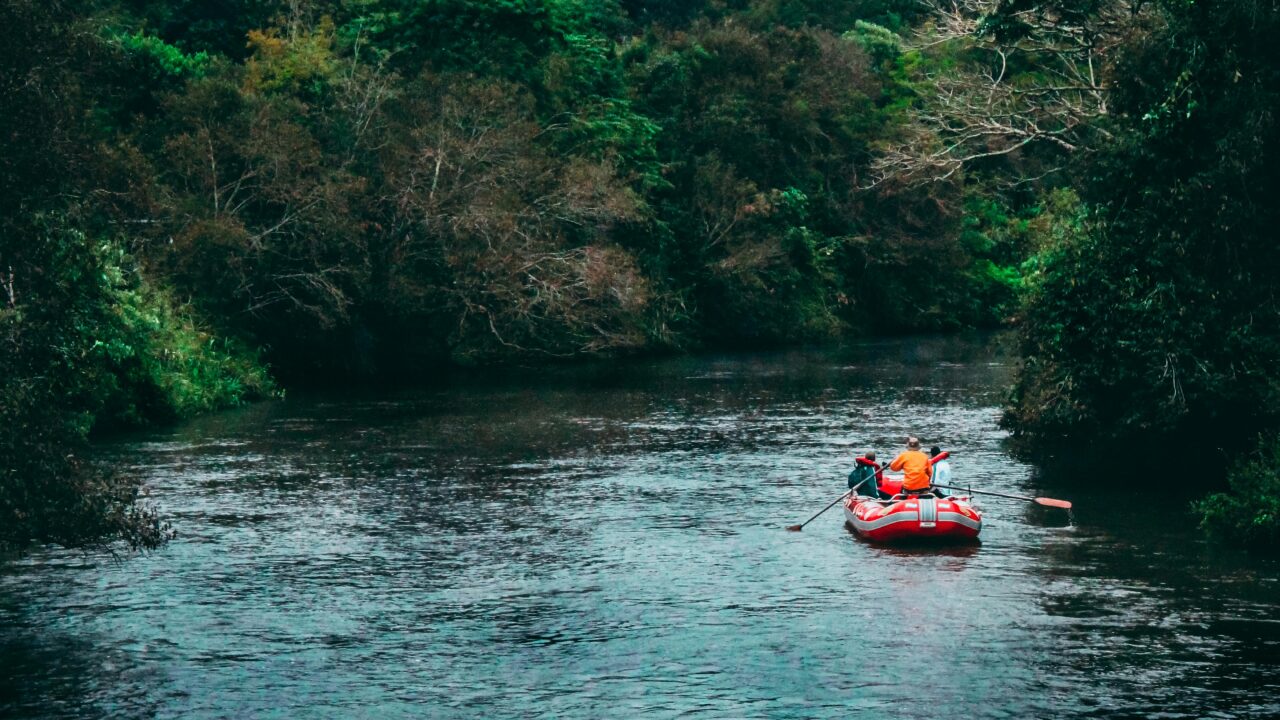 Three Persons Riding Red Inflatable Raft