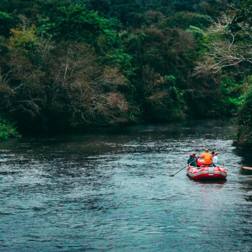 Three Persons Riding Red Inflatable Raft