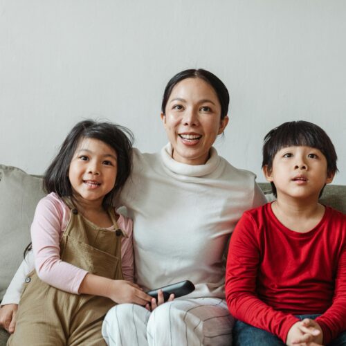 Happy ethnic mother with little children watching TV on sofa