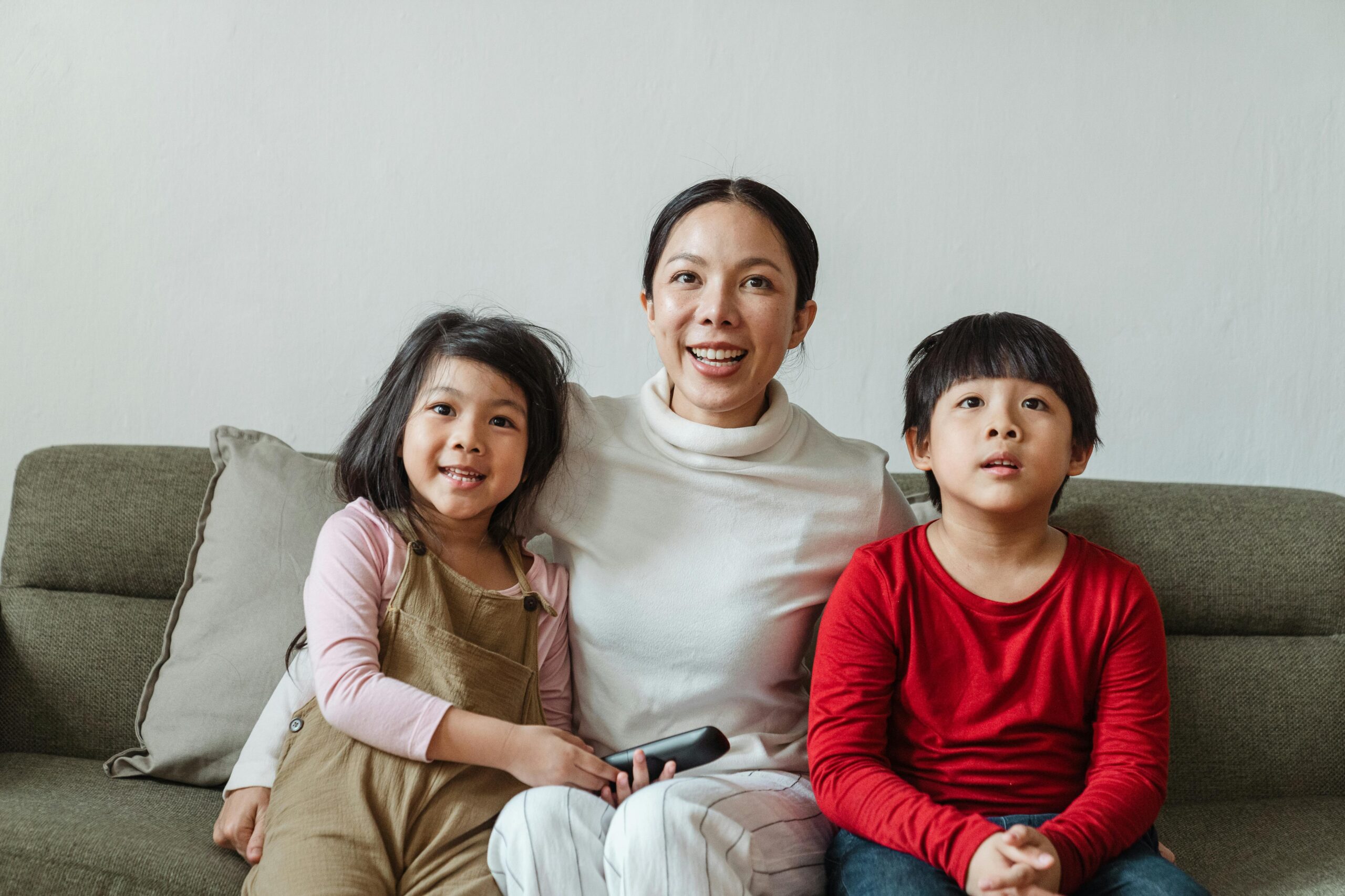 Happy ethnic mother with little children watching TV on sofa