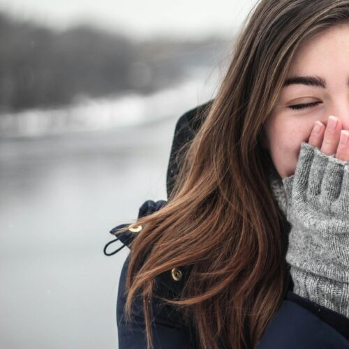 Woman in Black Hooded Down Jacket Covering Her Face With Grey Fingerless Gloves