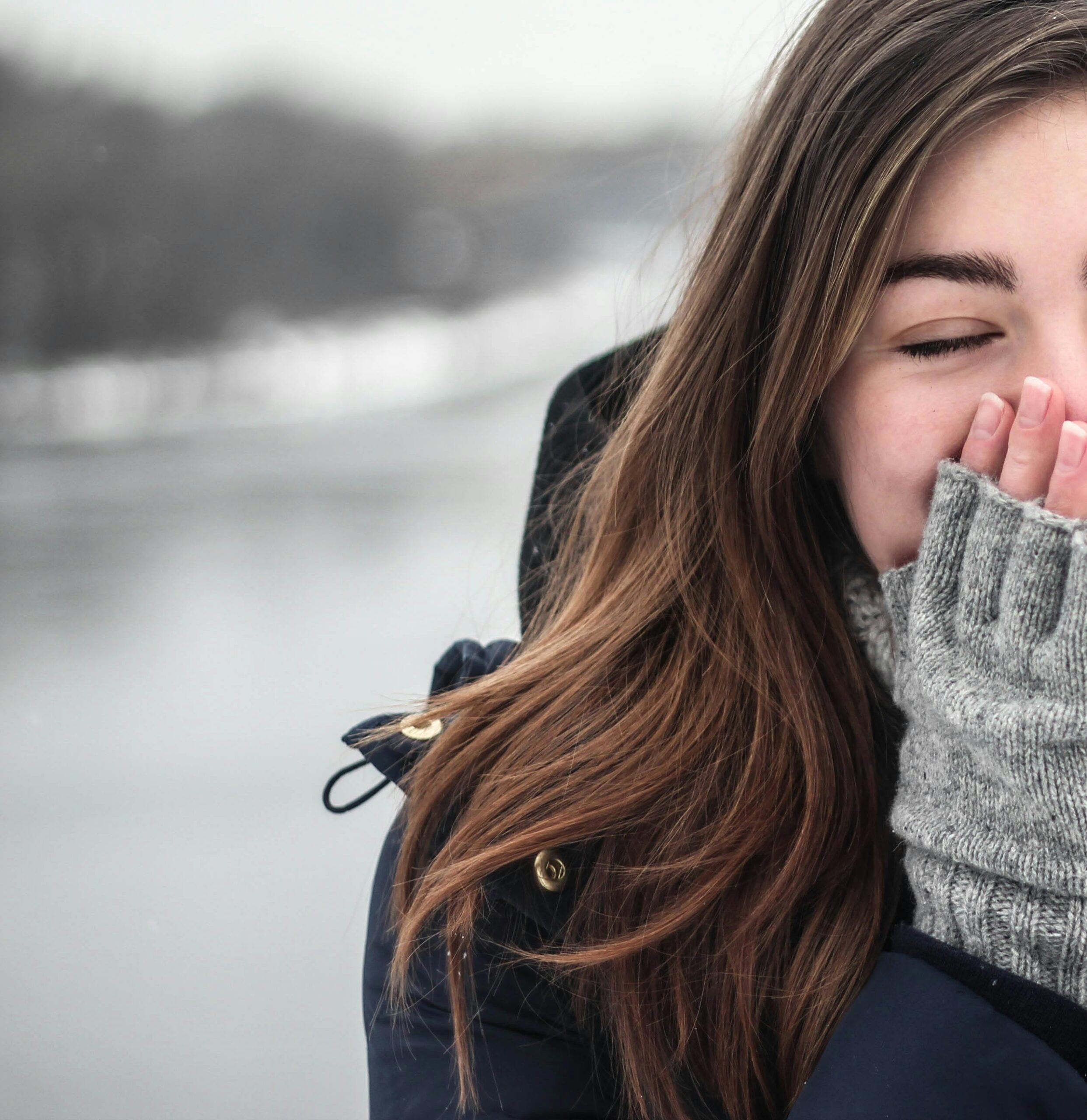 Woman in Black Hooded Down Jacket Covering Her Face With Grey Fingerless Gloves