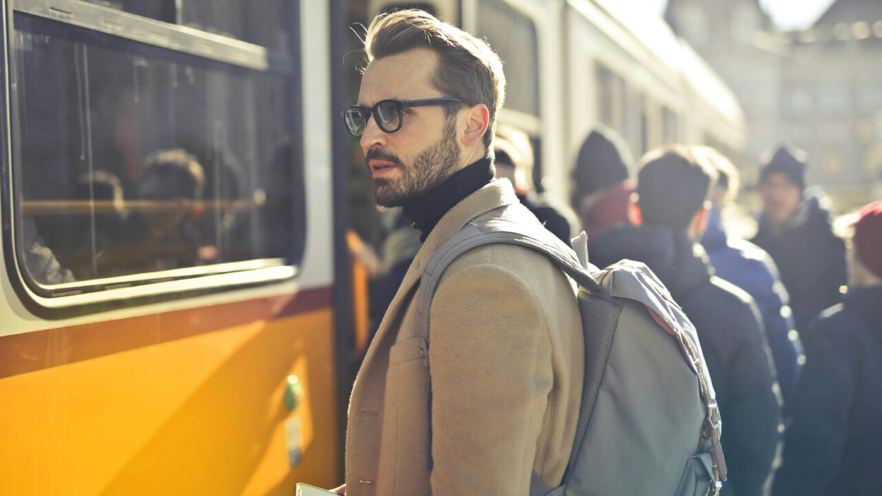 Man in Brown Coat and Gray Backpack Posing for a Photo