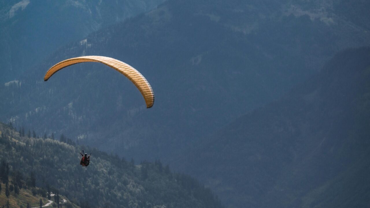 Person Riding Yellow Parachute over Mountain Range